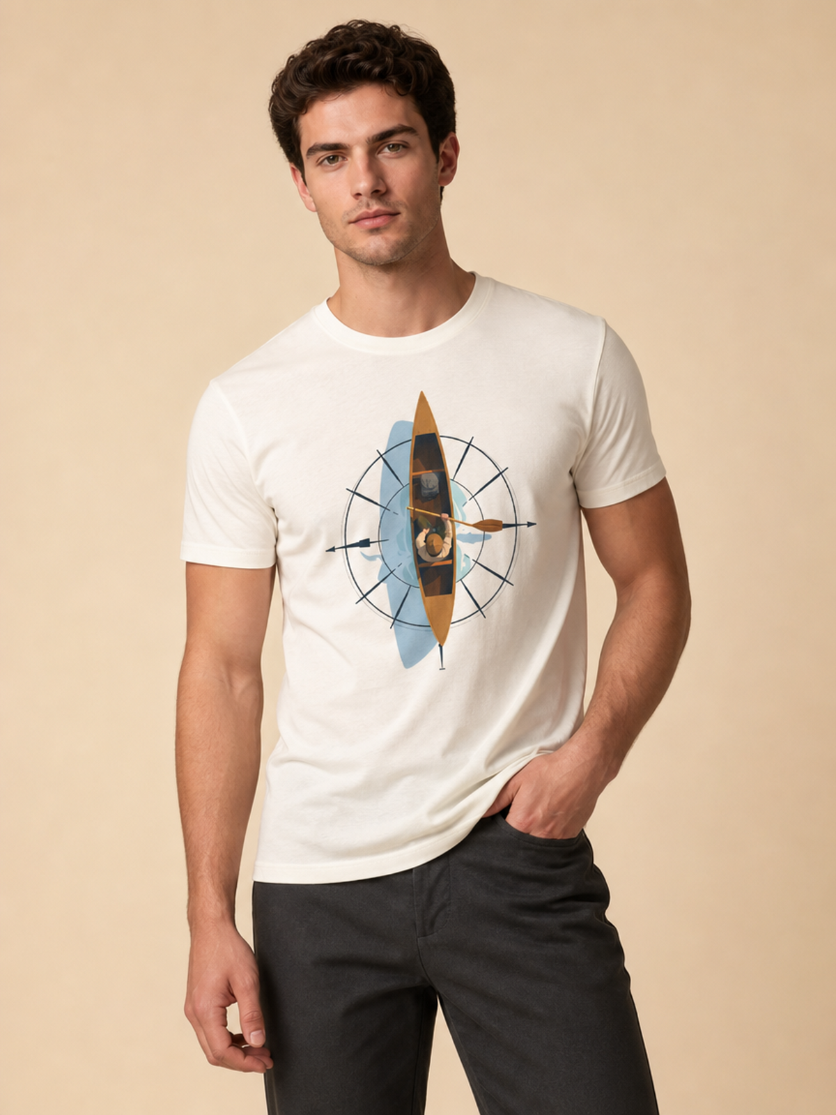 A man wearing a white crewneck t-shirt with a graphic print of a compass and a kayak, paired with dark gray pants, against a solid beige background.