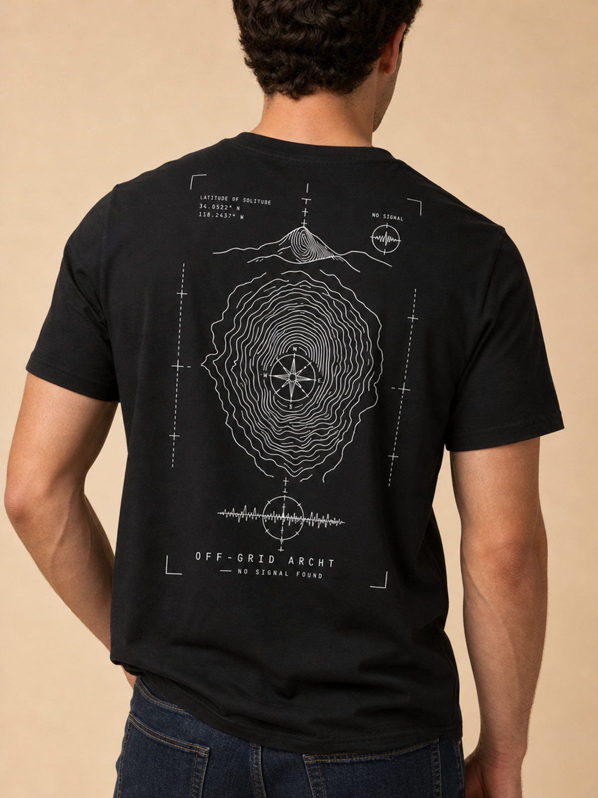 A man viewed from behind wearing a black t-shirt with a white topographic map and compass graphic on the back, paired with blue jeans, set against a solid beige background.